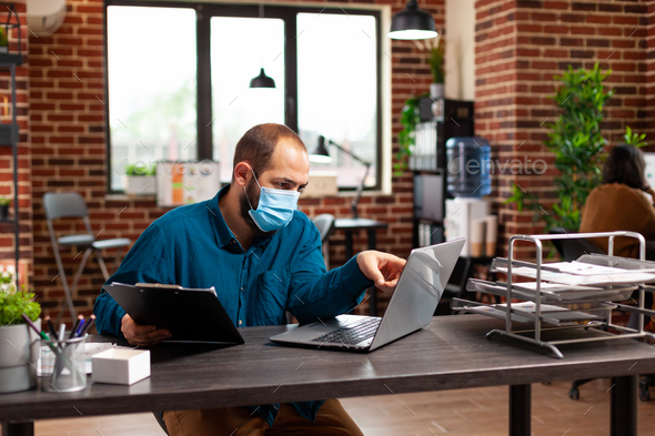 Bookkeeper man with medical protective face mask against coronavirus working at management strategy