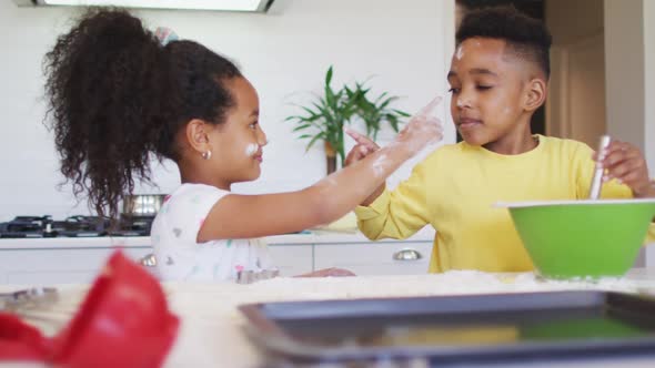 Happy, messy african american siblings making cookies together in kitchen alt