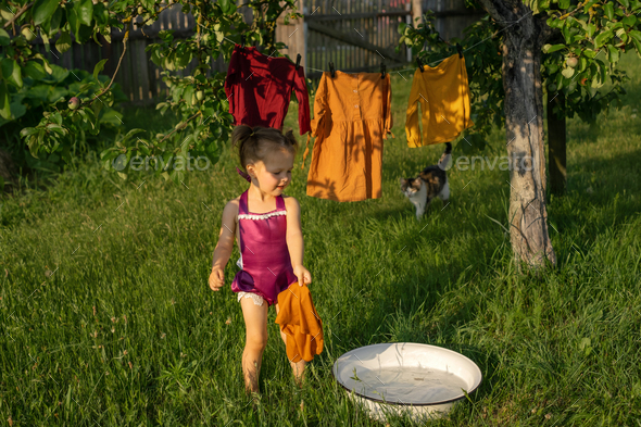 A girl splashes in a basin with soapy water, washes clothes and hangs clothes