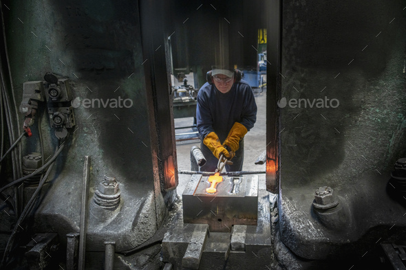Engineer forging titanium parts in hammer press in industrial forge