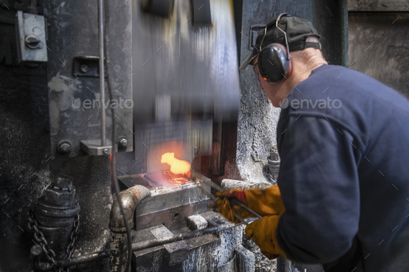 Engineer forging titanium parts in hammer press in industrial forge