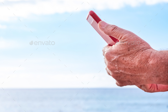 Close-up on human male hands holding a smart phone with red cover. Addiction, elderly man