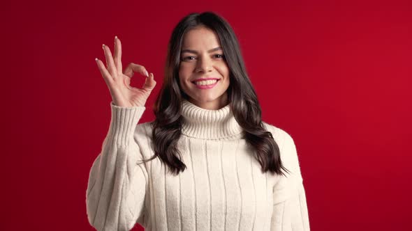 Young Latin Woman with Perfect Make-up in Sweater Making OK Sign Over Red  alt