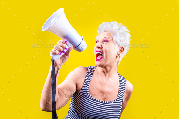 Senior woman screaming loudly in a megaphone on yellow background