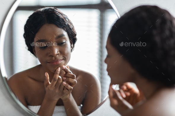 Beautiful black woman touching her face, pressing pimple