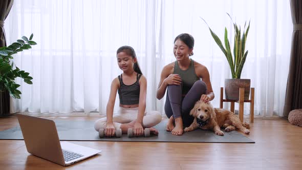 Happy Asian family mom and little daughter lifting dumbbell follow video from laptop