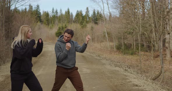 a girl and a guy run along a forest road in autumn, they stop and the guy shows how to box alt