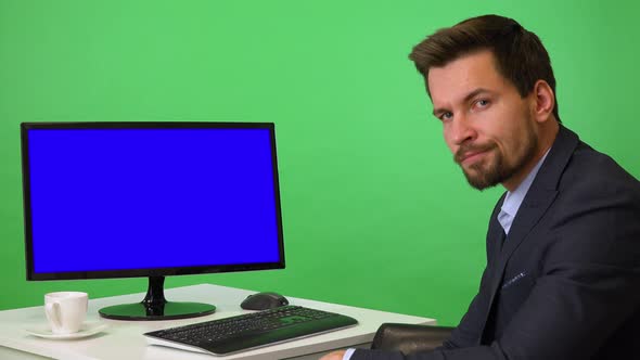 A Young Businessman Sits in Front of a Computer and Shows a Thumb Down To the Camera - Green Screen alt