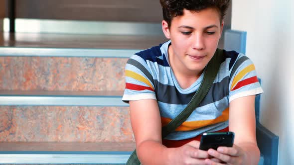 Schoolboy sitting on staircase and using mobile phone alt