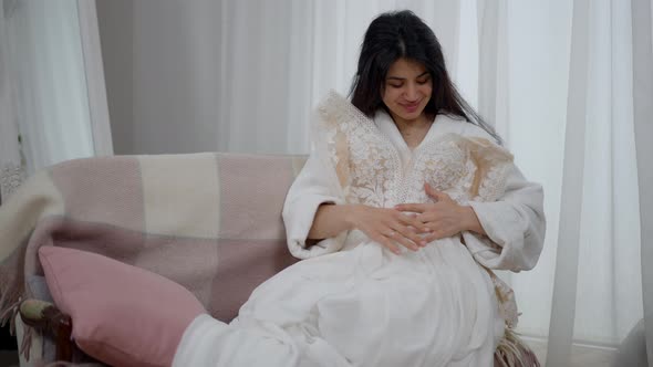 Front View Portrait of Happy Smiling Middle Eastern Bride Holding Wedding Dress on Sitting on Couch alt