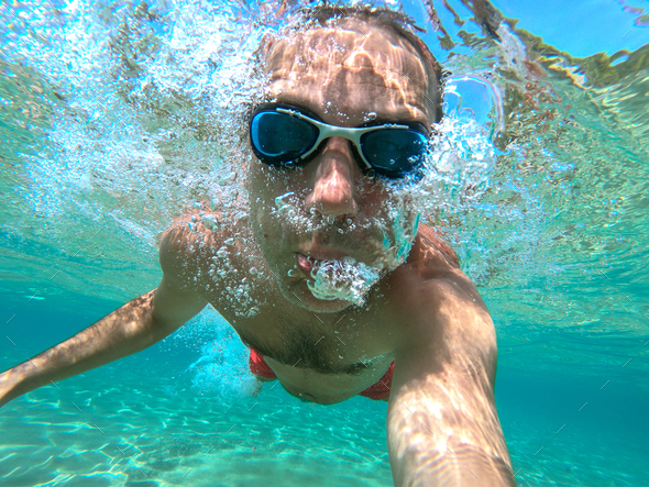 Underwater view of a young diver man swimming in the sea. Air bubbles coming out from mouth and nose