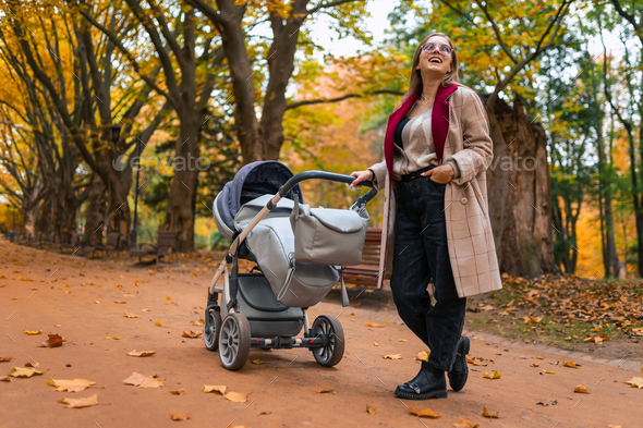 Smiling mom with baby stroller in the park