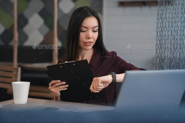 Portrait of woman checking time on watch on hand and document folder