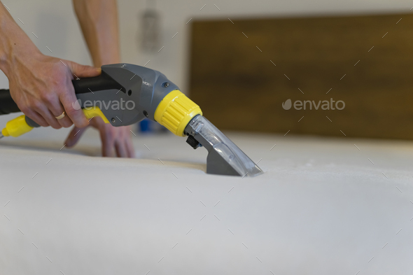 Employee of cleaning company cleans and disinfecting the mattress using a washing vacuum cleaner.