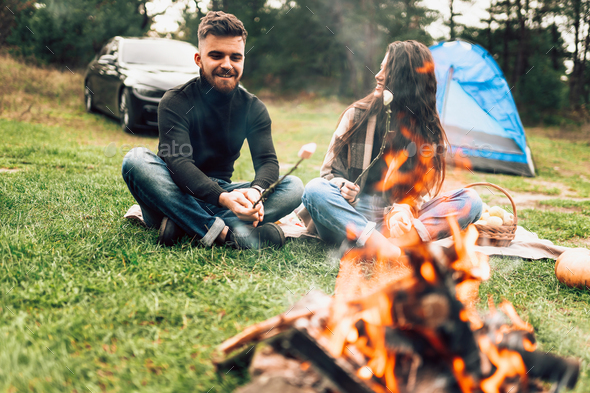 Romantic couple in nature near the campfire roasting marshmallows