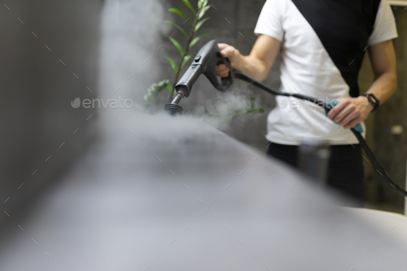 Worker of a cleaning company is cleaning the tiles in the bathroom with steam