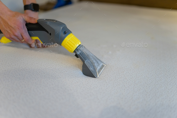 Employee of cleaning company cleans and disinfecting the mattress using a washing vacuum cleaner.