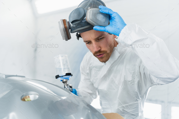 Professional car painter in the painting booth takes off his protective mask to check the quality