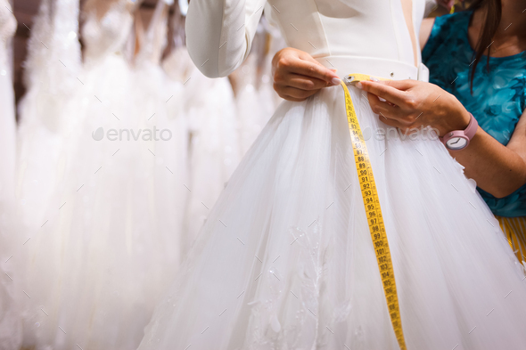 Consultant of the salon of wedding dresses takes measurements of the client\'s waist