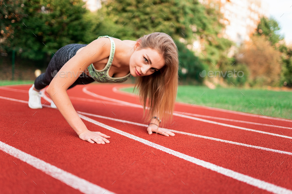 Athletic girl stands in the plank at the stadium runway Stock Photo by  borodai