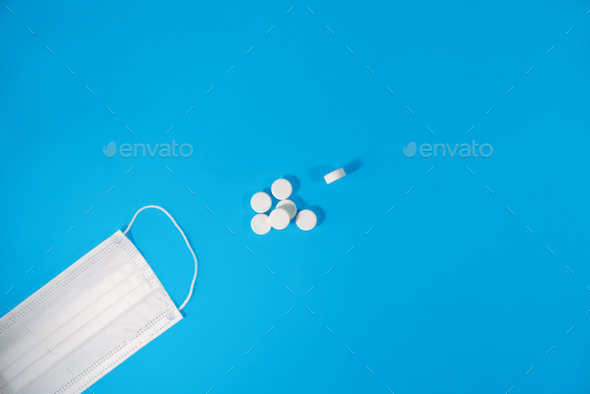 Medical face mask and many antibiotic pills on a blue background, copy space. Means of protection