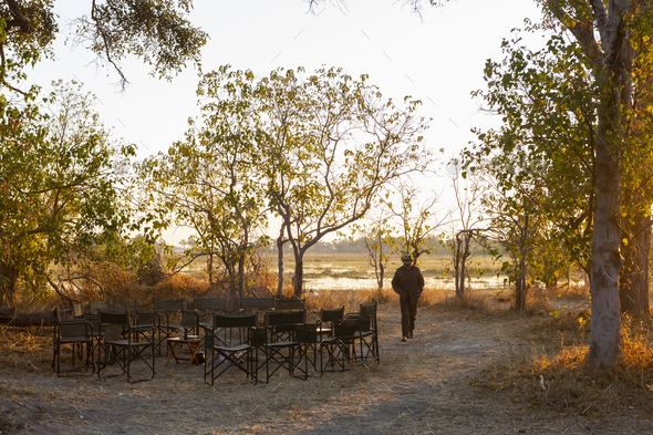 A man walking on a path at a safari camp by a water pool