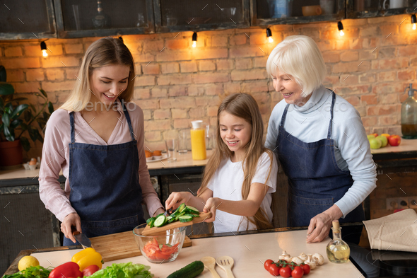 Beautiful family cooking in kitchen. Young girl putting cucumbers into ...