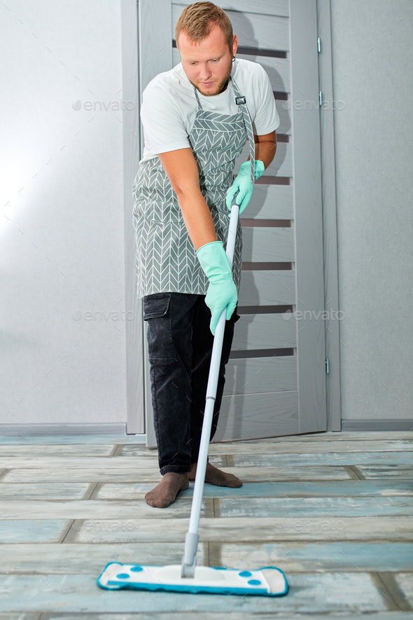 Bearded man in gloves with mop in hand cleaning floor in the house