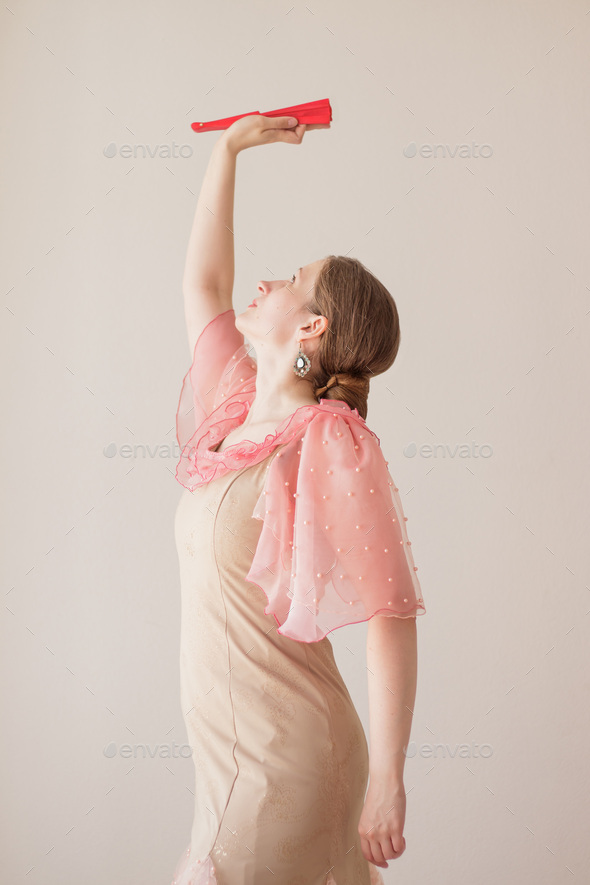 Beautiful young woman in beige, pink dress dancing flamenco.Hand with red fan raised up.