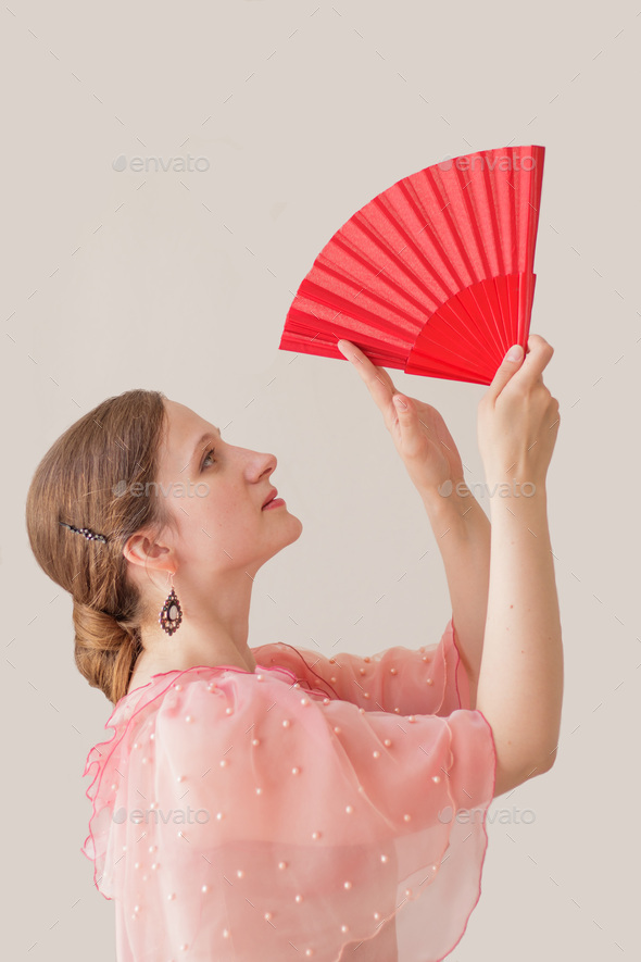 Profile of beautiful young woman in pink dress dancing flamenco. Hands with red fan raised up.