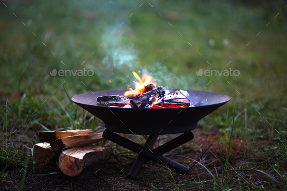 The flame of the fire burns in a metal fire bowl - warm your hands by the fire, stir the firewood
