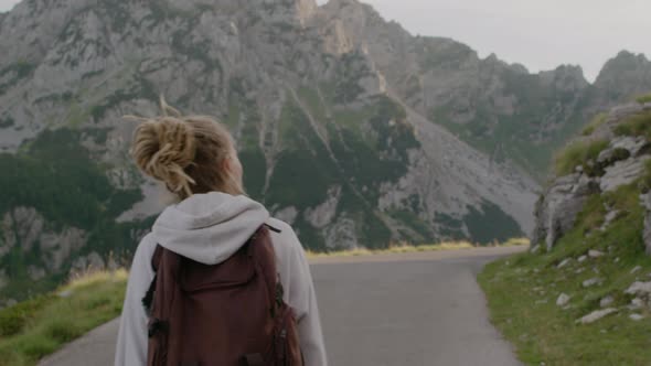 Back view of travel woman with dreadlocks and backpack walking through the national park alt