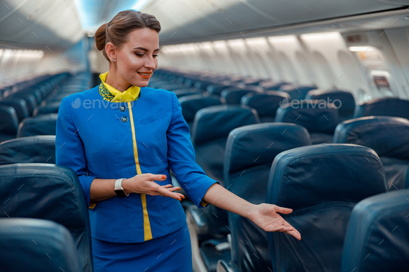 Woman stewardess pointing at passenger seat in airplane cabin