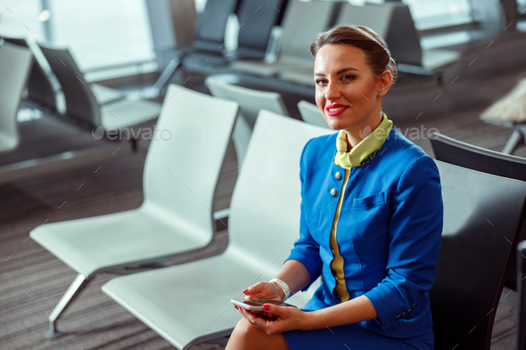 Joyful woman stewardess sitting on chair in airport departure lounge ...
