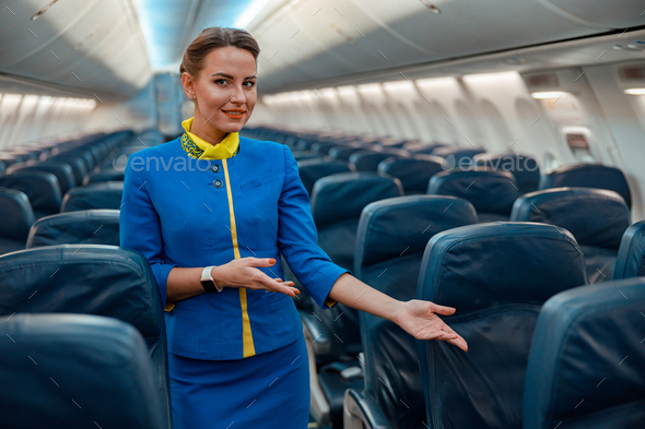 Female flight attendant pointing at passenger seat in airplane cabin