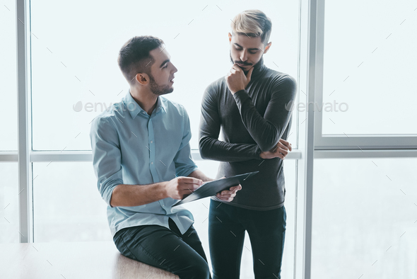 Two focused male co-workers deep in discussion together, while standing in a modern office - Stock Photo - Images