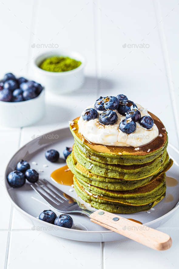 Matcha tea green pancakes with coconut cream, blueberries and maple syrup, white background.