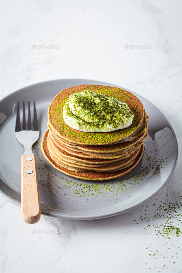 Stack of vegan pancakes with coconut cream and matcha powder on gray plate.