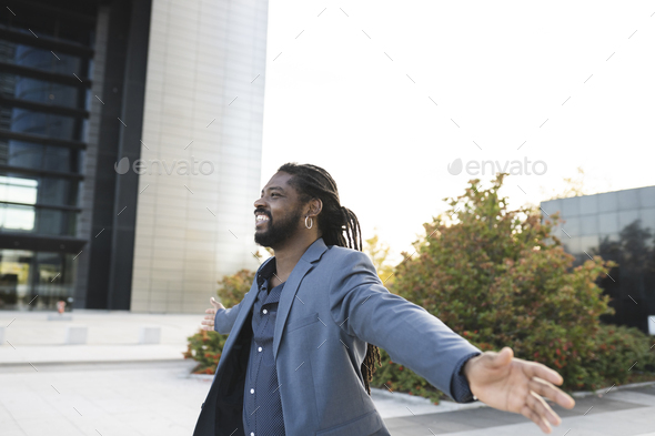 African American man in suit keeps his arms open while smiling stands on the city streets