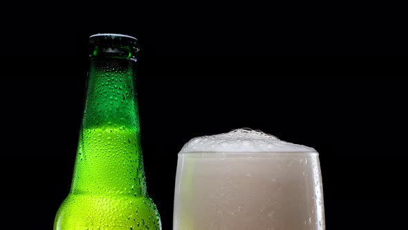 A Glass of Beer with Foam Next to a Green Beer Bottle