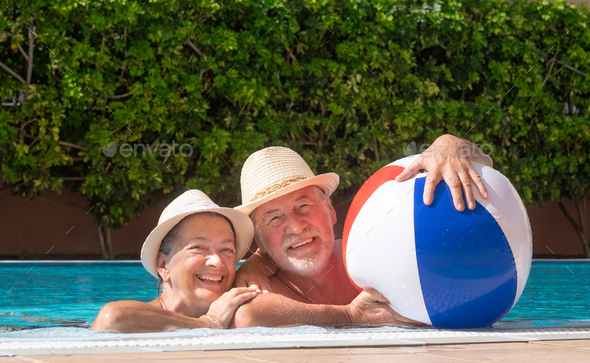Happy senior caucasian couple floating in outdoor swimming pool playing with inflatable balloon