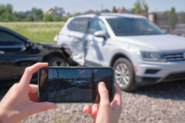 Stressed driver taking picture on sellphone camera of smashed vehicle calling for emergency service