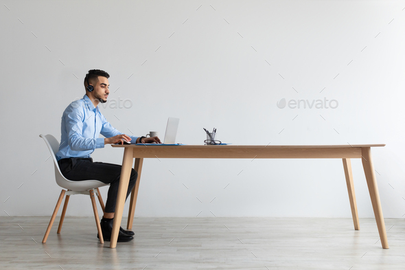 Arab man using laptop wearing headset sitting at desk
