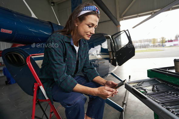 Woman engine mechanic sitting in front of the private jet airplane in hangar
