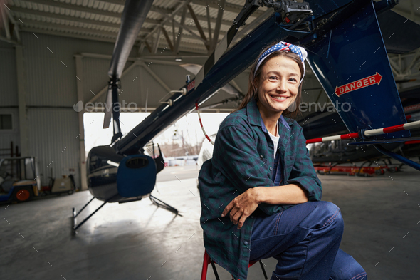 Beautiful smiling brunette airframe engineer sitting in the aviation garage - Stock Photo - Images