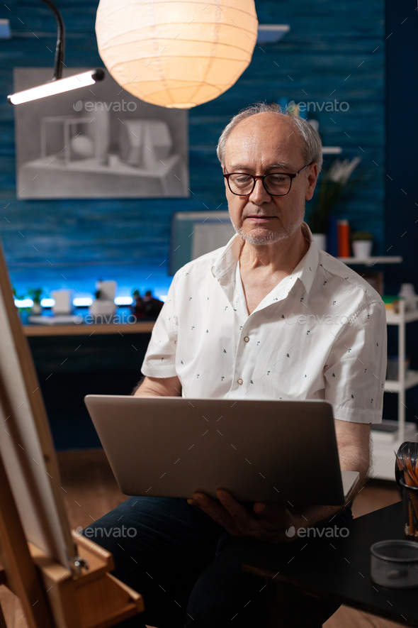 Portrait of older man looking to sell artwork on internet using portable computer