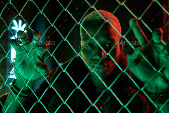 Young sad man of African ethnicity standing behind bars