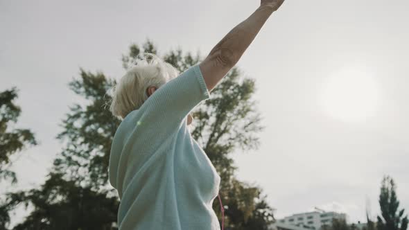 Senior Retired Woman Enjoying Freedom of Retirement. Outstretched Hands in the Park, Low Angle Shot alt
