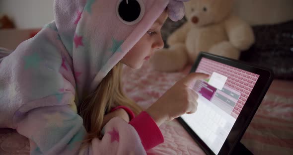 Little Girl is Playing in the Children's Room in Unicorn Costume Using Tablet alt
