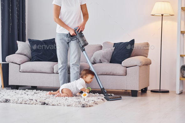 Using of the vacuum cleaner. Mother with her little daughter is indoors ...